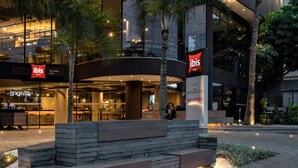 Een modern hotel met een opvallend ‘ibis’ bord, een terras en palmbomen.