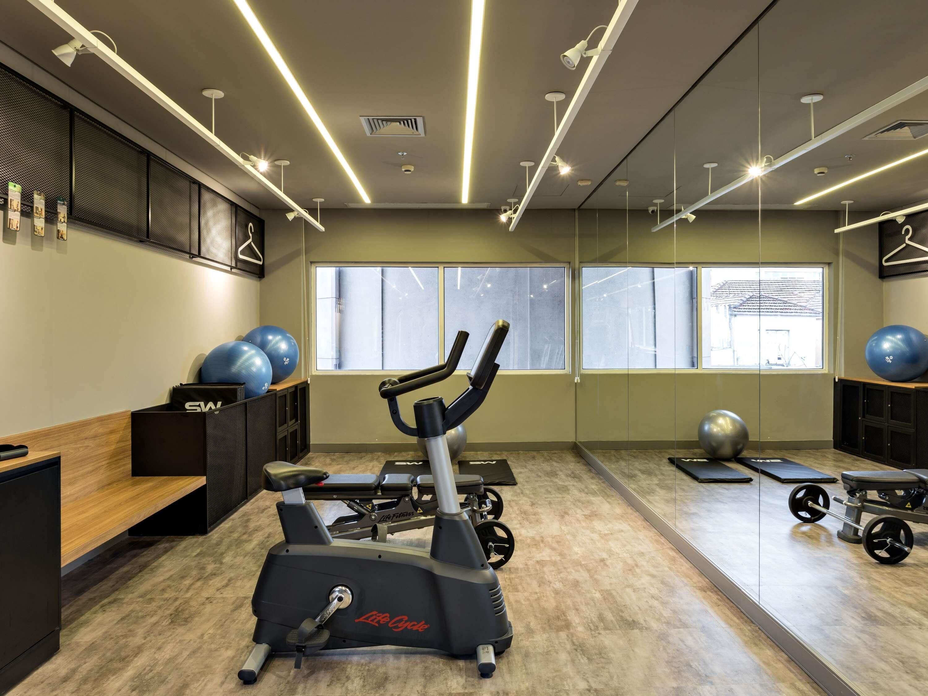 A gym with exercise equipment, a mirrored wall, and large windows.