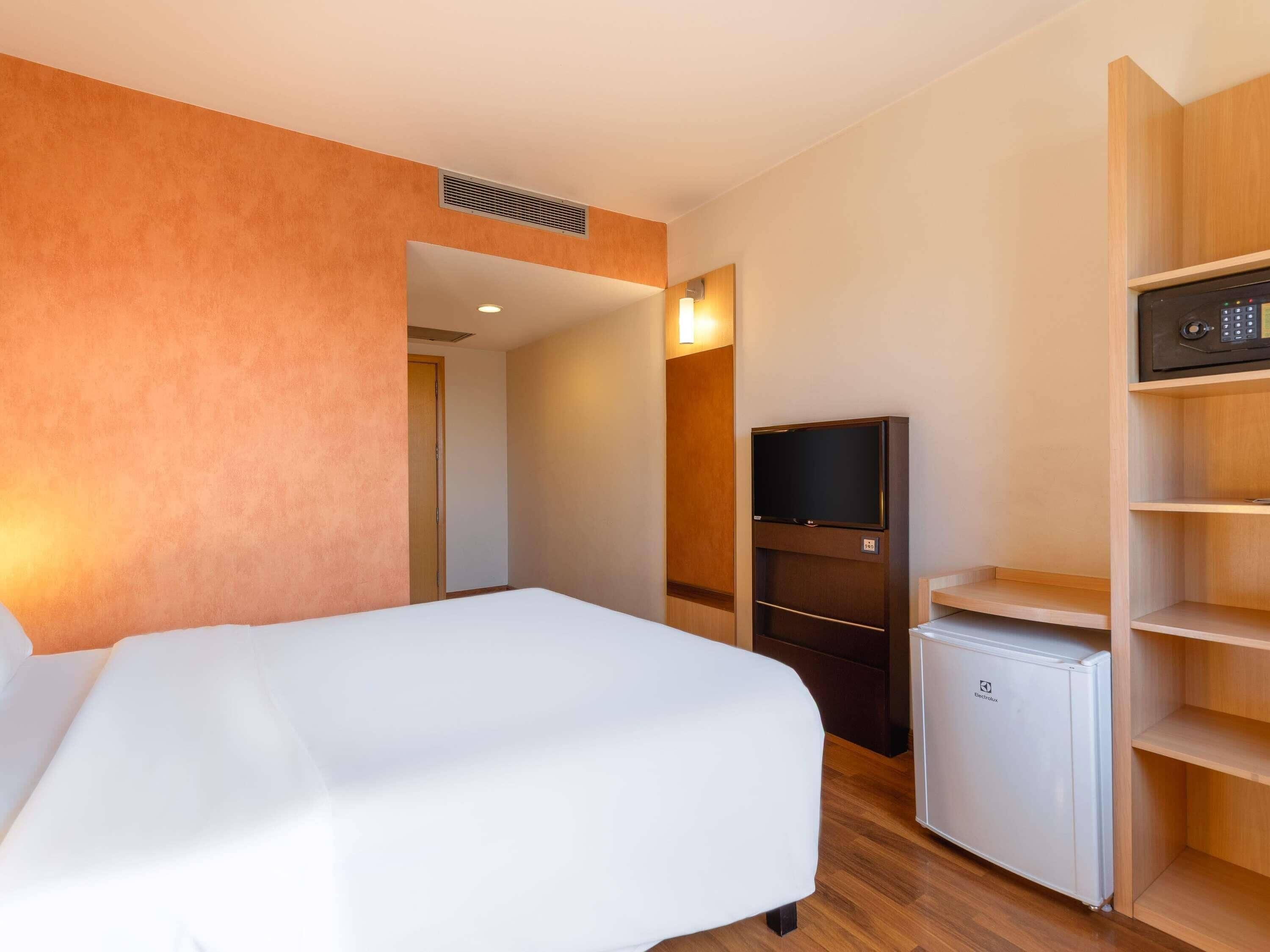 Een hotelkamer met een bed, een televisie, een minibar en een houten plankunit.