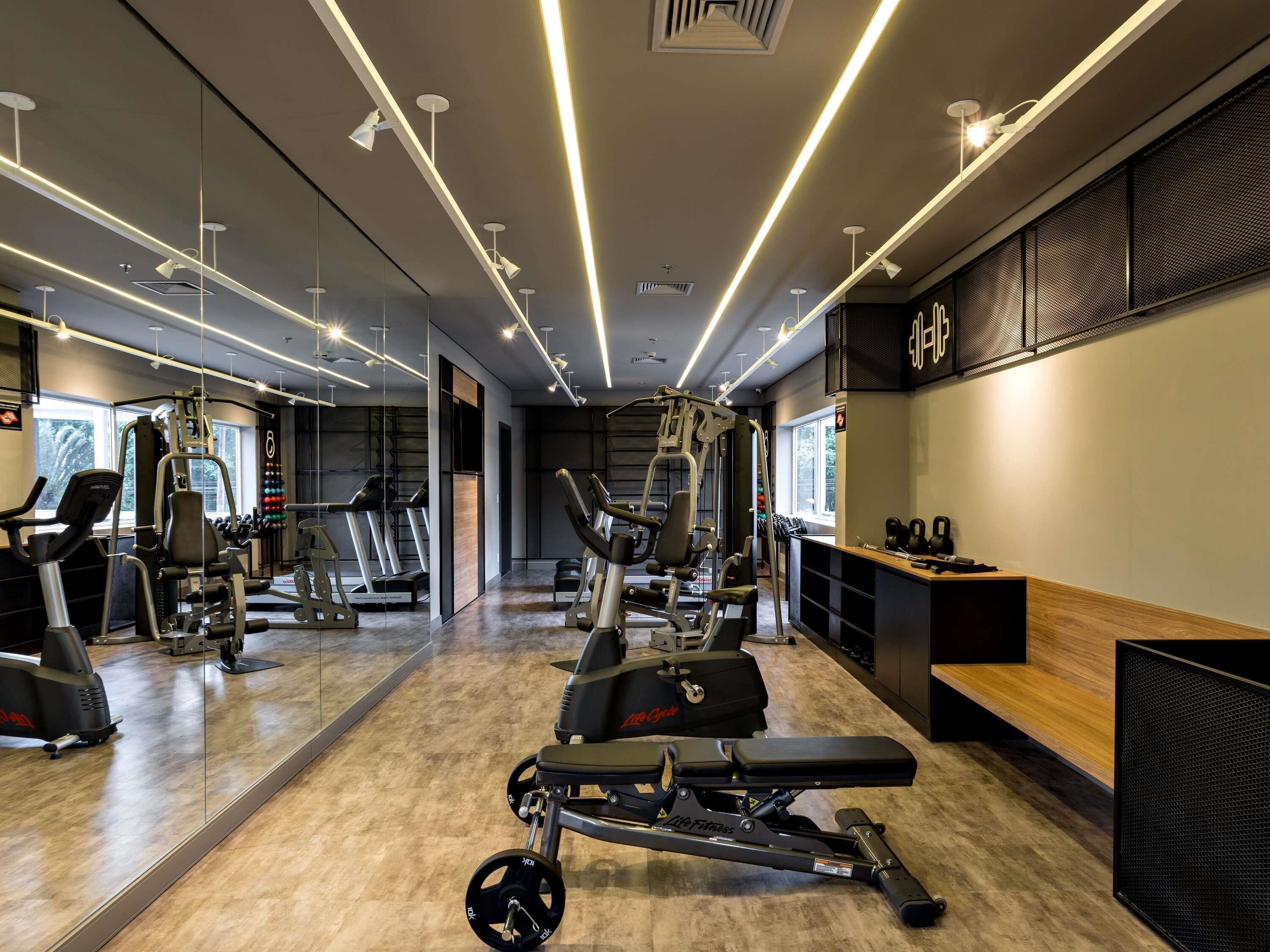 A gym with exercise equipment, mirrors, and a wooden bench.