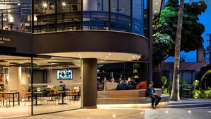 Een modern gebouw met een gebogen glazen gevel, een terras en palmbomen.