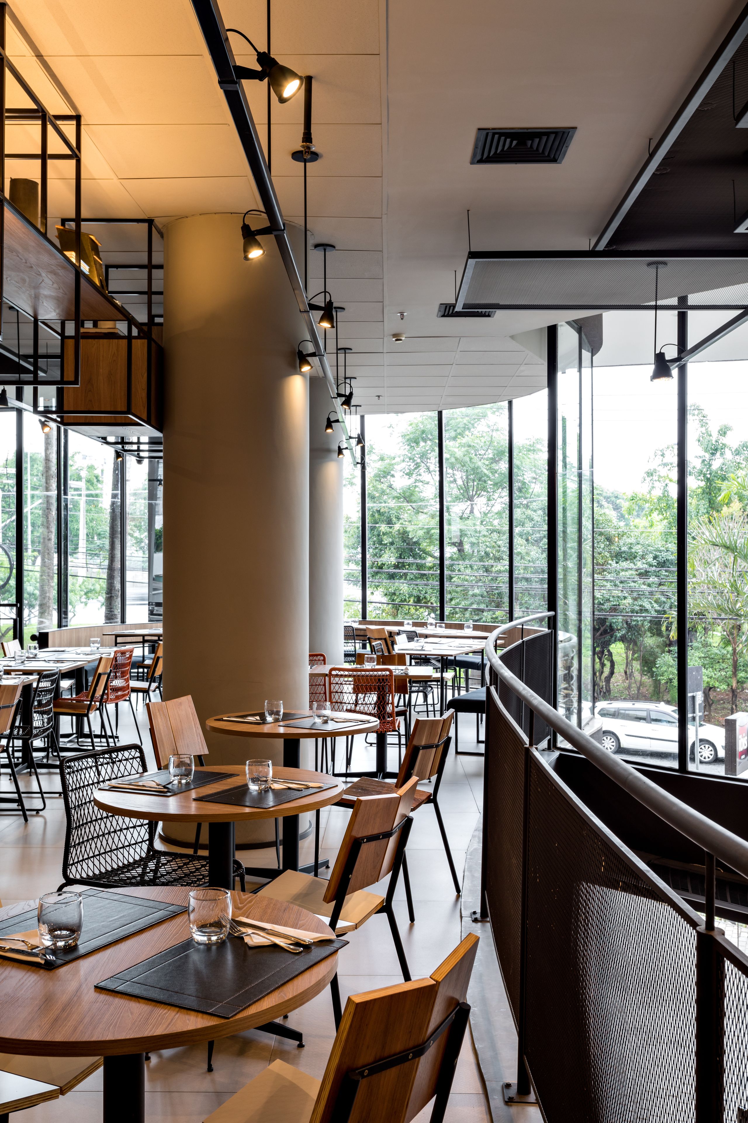 Un restaurante moderno con mesas redondas, sillas de madera y grandes ventanales que ofrecen vistas al exterior.