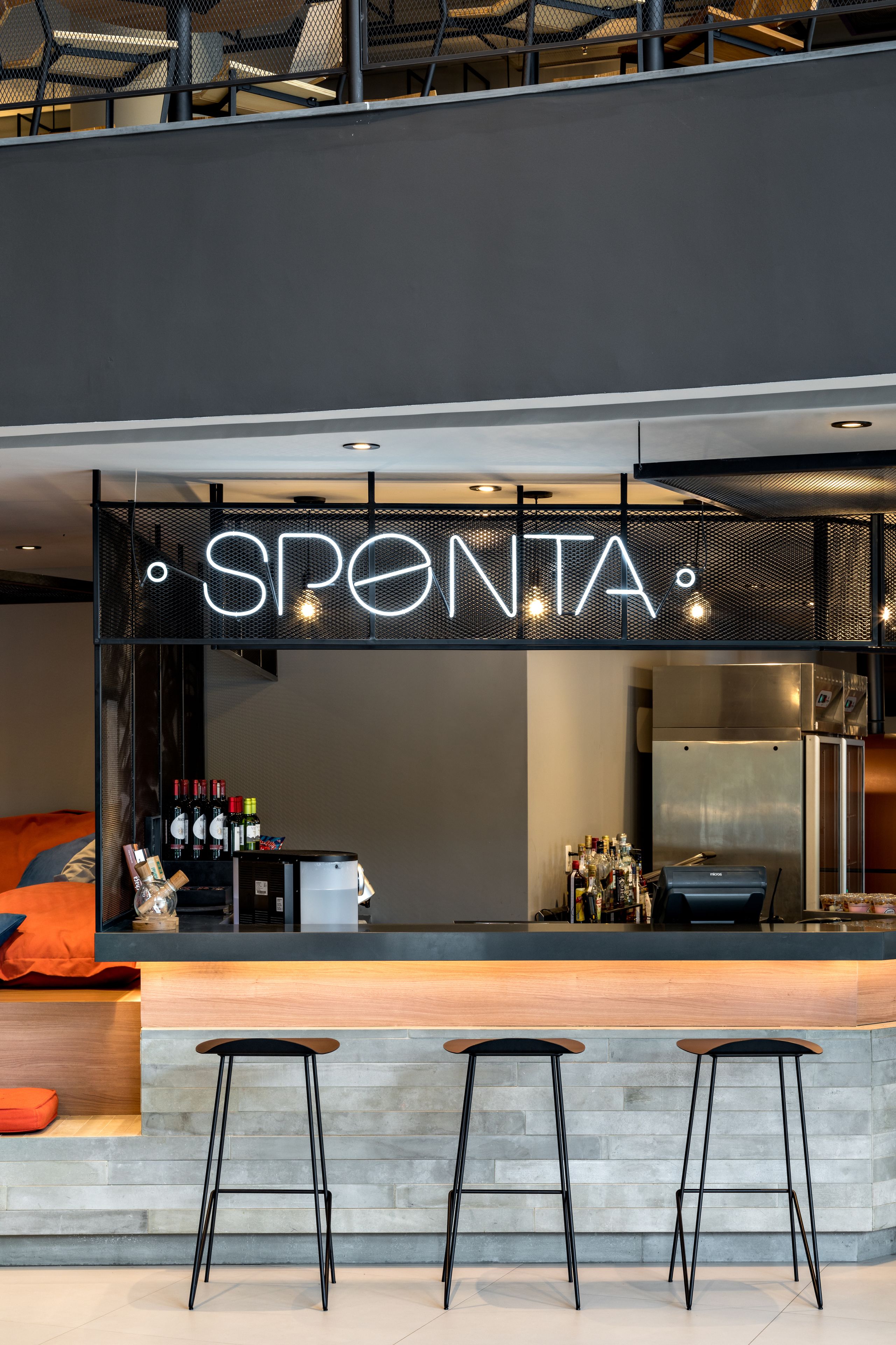 Un coin bar agrémenté d’un panneau néon sur lequel on peut lire « SPONTA » et de deux tabourets.