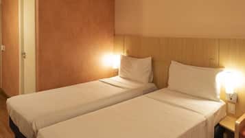 A hotel room with two single beds, wooden headboard, bedside lamps, and a door.