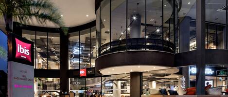 A modern hotel interior with a glass facade, a central atrium, and a seating area with a view of the lobby.
