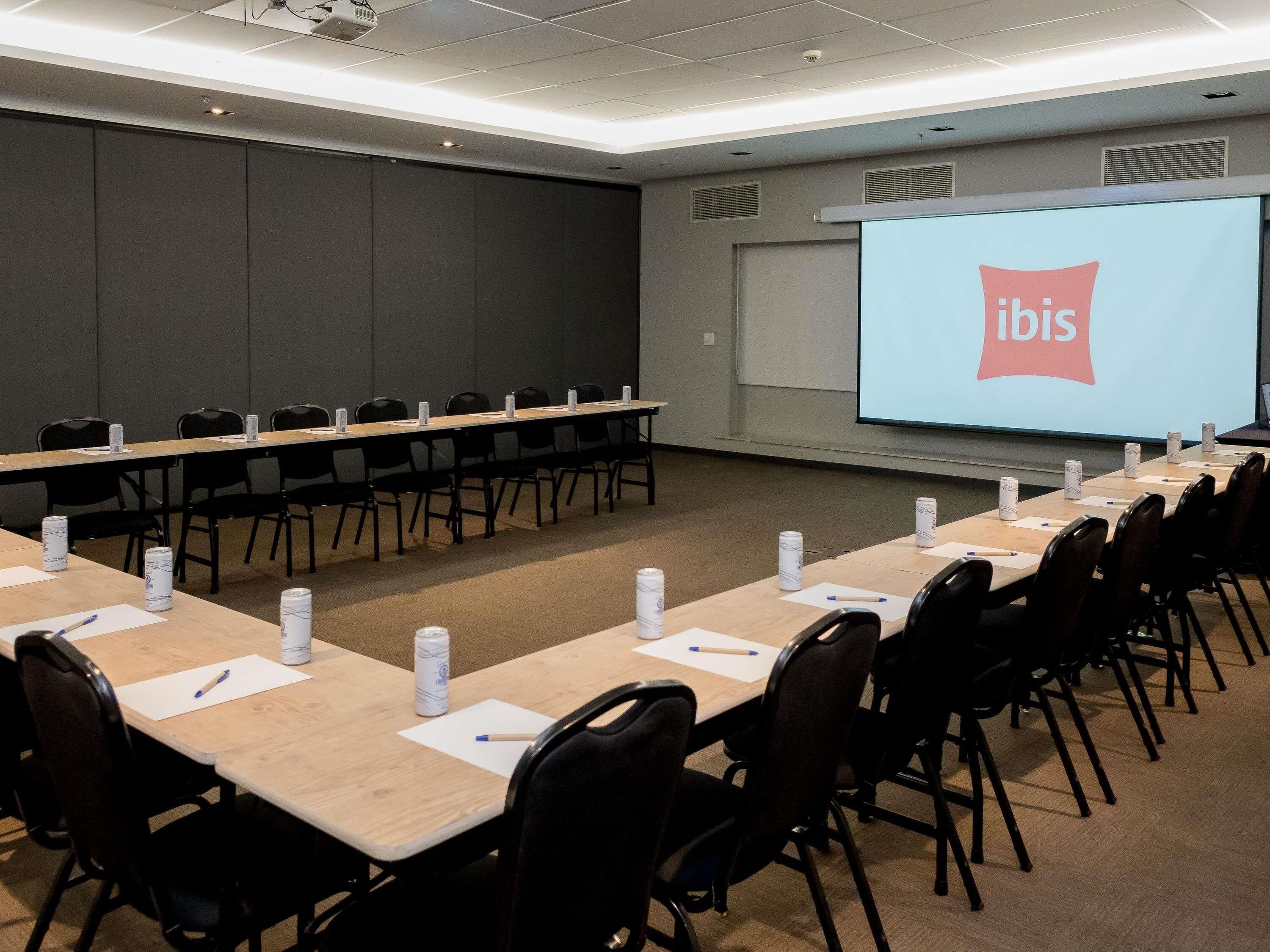A conference room with long tables, chairs, and a projector screen displaying the ibis logo.