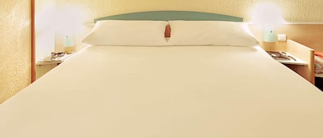 A neatly made bed with a green headboard, two bedside tables with lamps, and a wooden nightstand with a lamp.