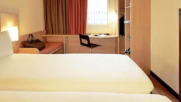 A hotel room with a large bed, a desk, a chair, a lamp, and a wardrobe.