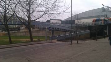 A pedestrian walkway with a bridge, a stadium, and a tram.