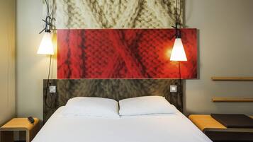 A hotel room with a large bed, two bedside tables, a headboard with a textured design, and a wall-mounted artwork above the bed.