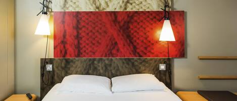 A hotel room with a large bed, two bedside tables, a headboard with a textured design, and a wall-mounted artwork above the bed.