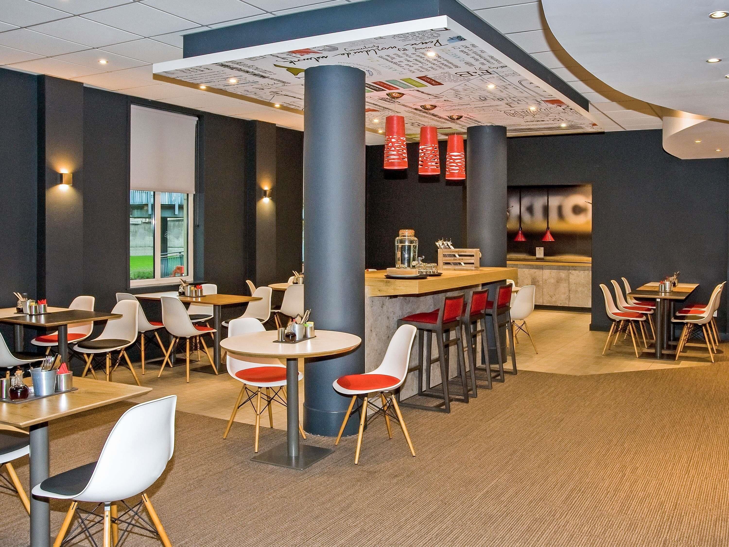 Een modern restaurant met ronde tafels en barkrukken, een centraal bargedeelte en een menukaart aan het plafond.