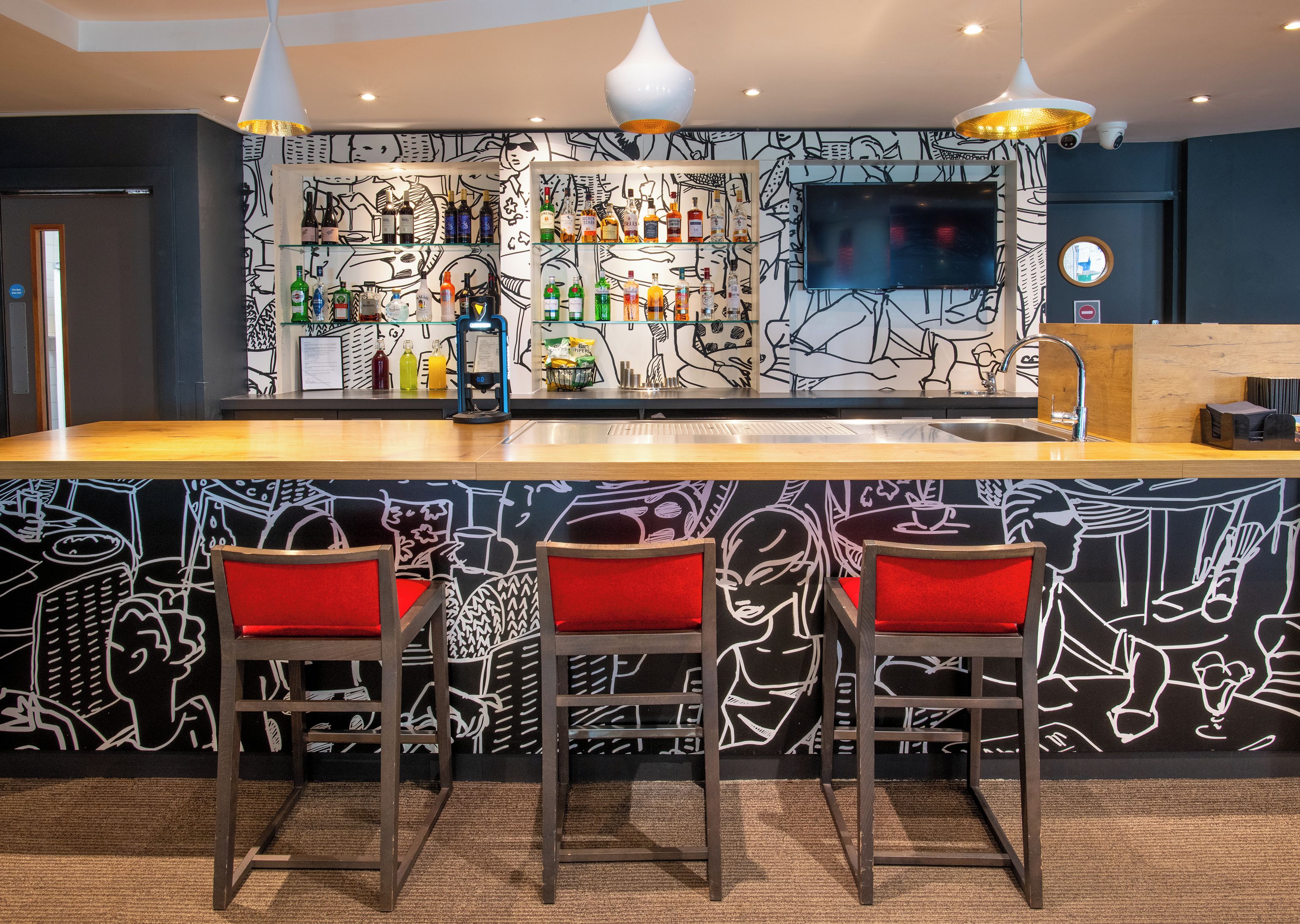 Una zona de bar con mostrador, taburetes y pared con un diseño abstracto en blanco y negro.