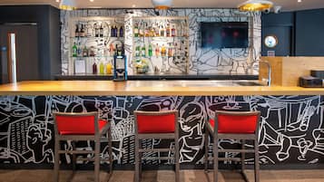 Una zona de bar con mostrador, taburetes y pared con un diseño abstracto en blanco y negro.