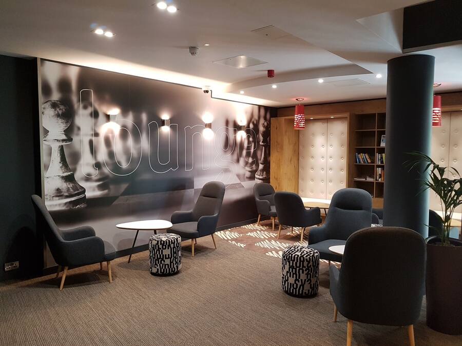 A lounge area with modern seating, a large wall mural, and a bookshelf.