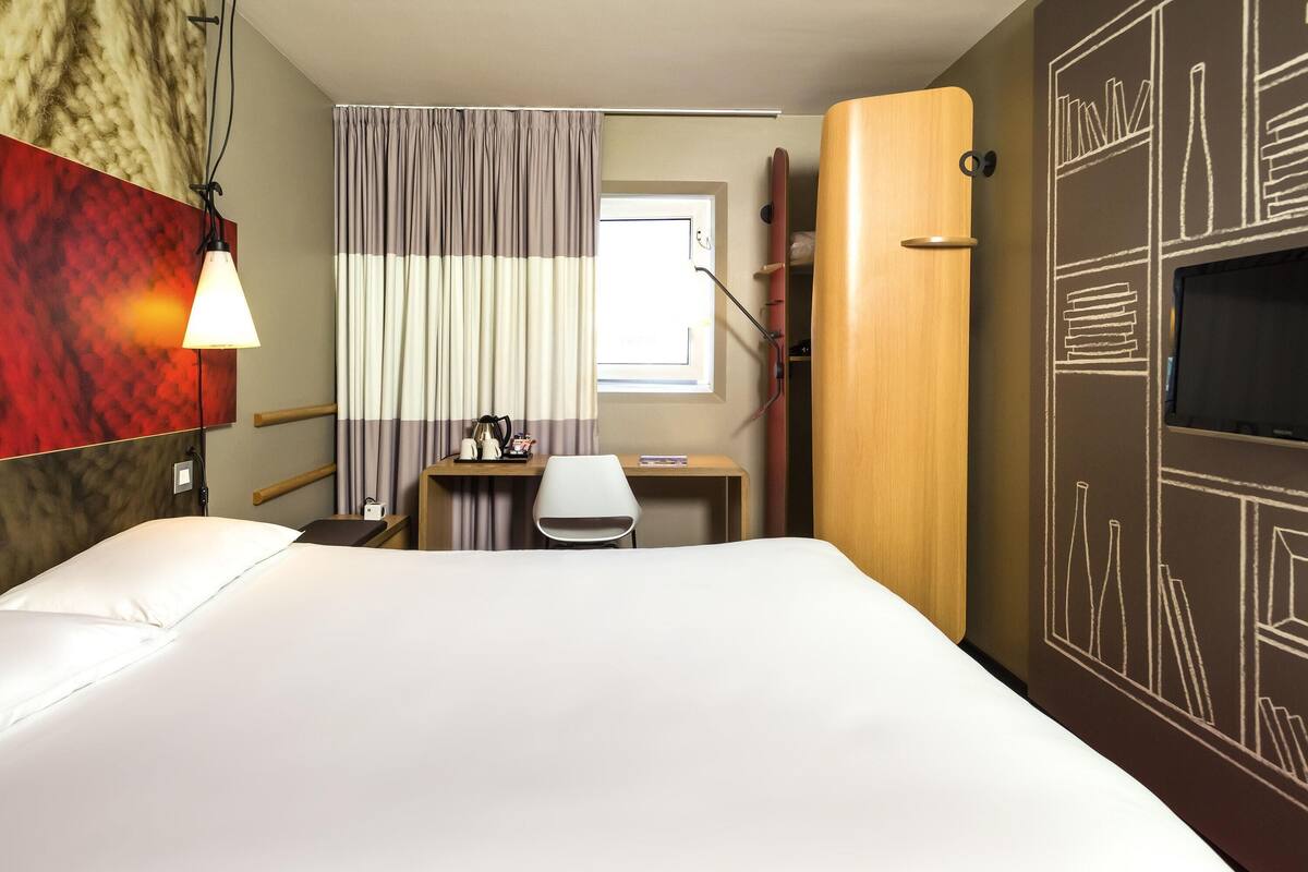 A hotel room with a bed, a desk, a chair, a TV, and a curtain.