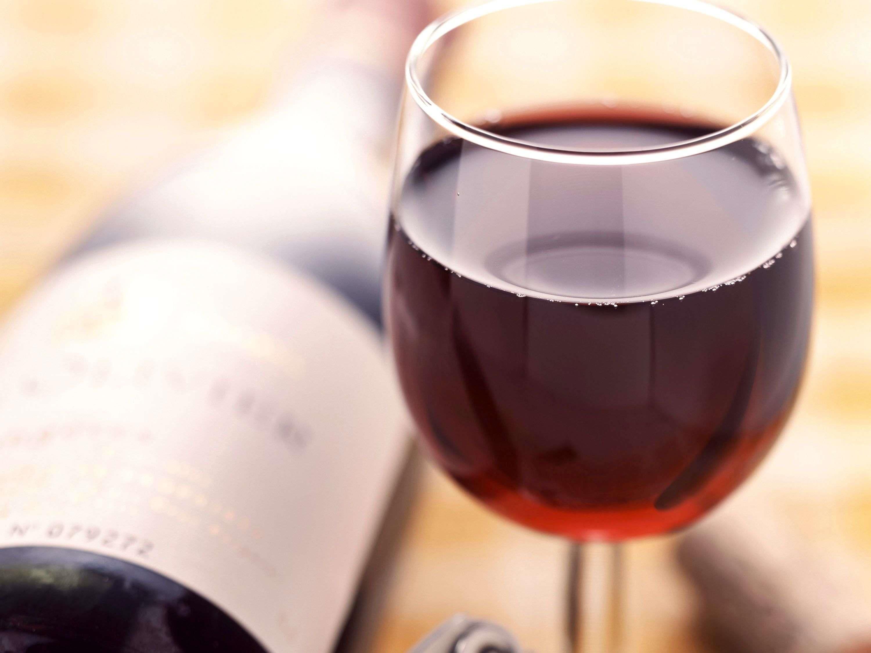 A wine glass filled with red wine, a bottle, and a blurred background.