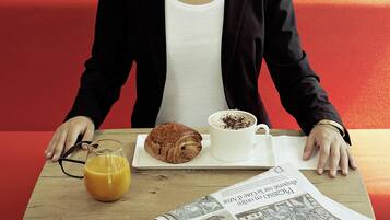 A person seated at a table with a croissant, a cup of coffee, and a glass of orange juice.