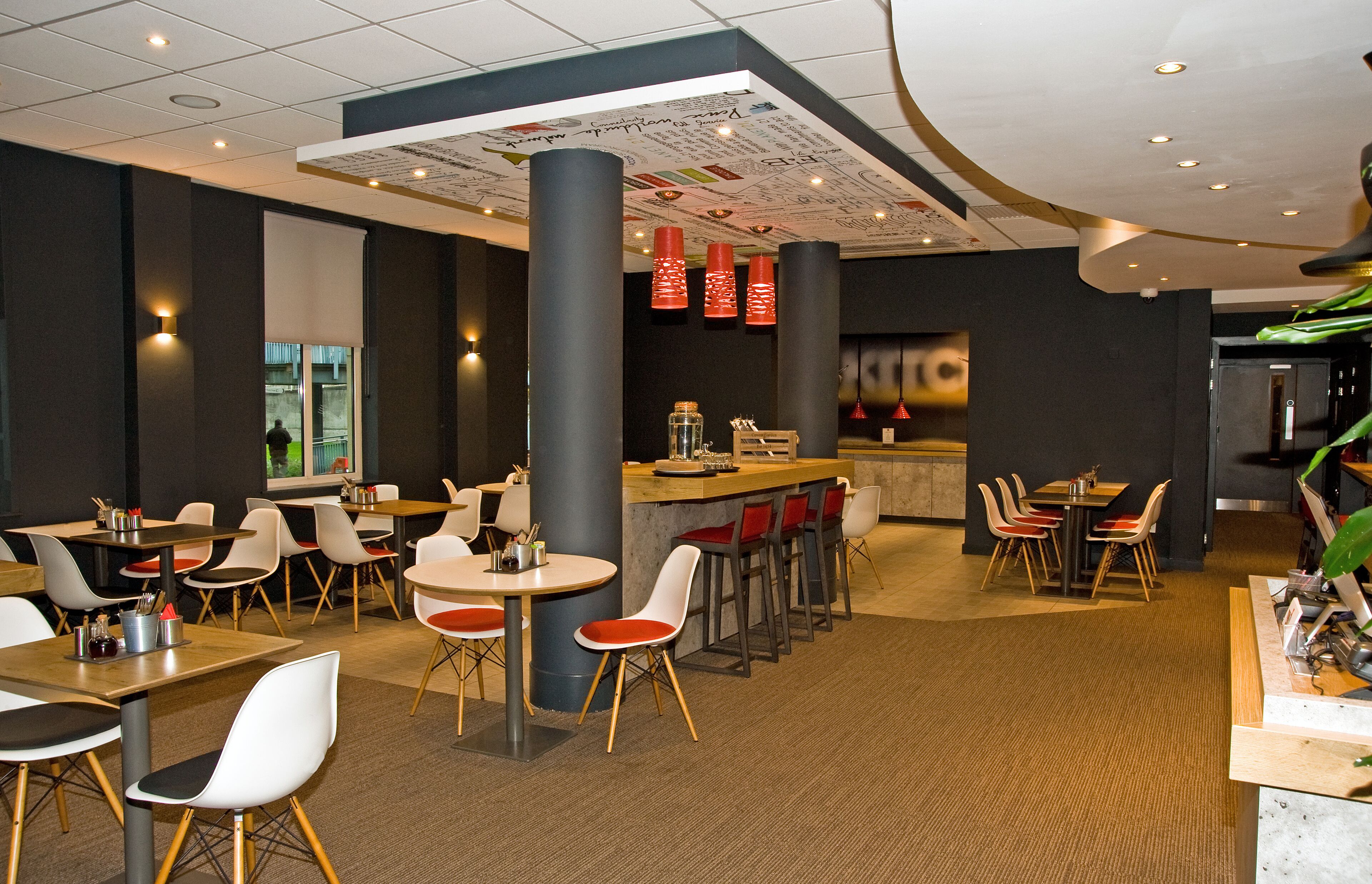 Un restaurant moderne avec des tables et des chaises rondes, un bar et une vue sur le paysage urbain grâce à de grandes fenêtres.