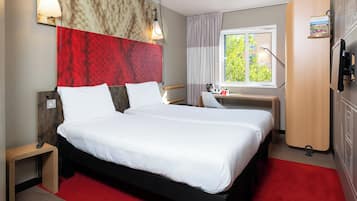 Een hotelkamer met een groot bed, een bureau, een stoel, een kledingkast en een raam met uitzicht op groen.