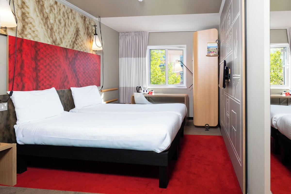 A hotel room with a bed, a desk, a chair, a wardrobe, and a window with a view of greenery.
