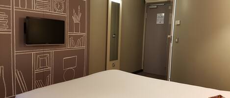 Habitación de hotel con una cama grande, un televisor de pantalla plana montado en la pared y una puerta que da a un pasillo.