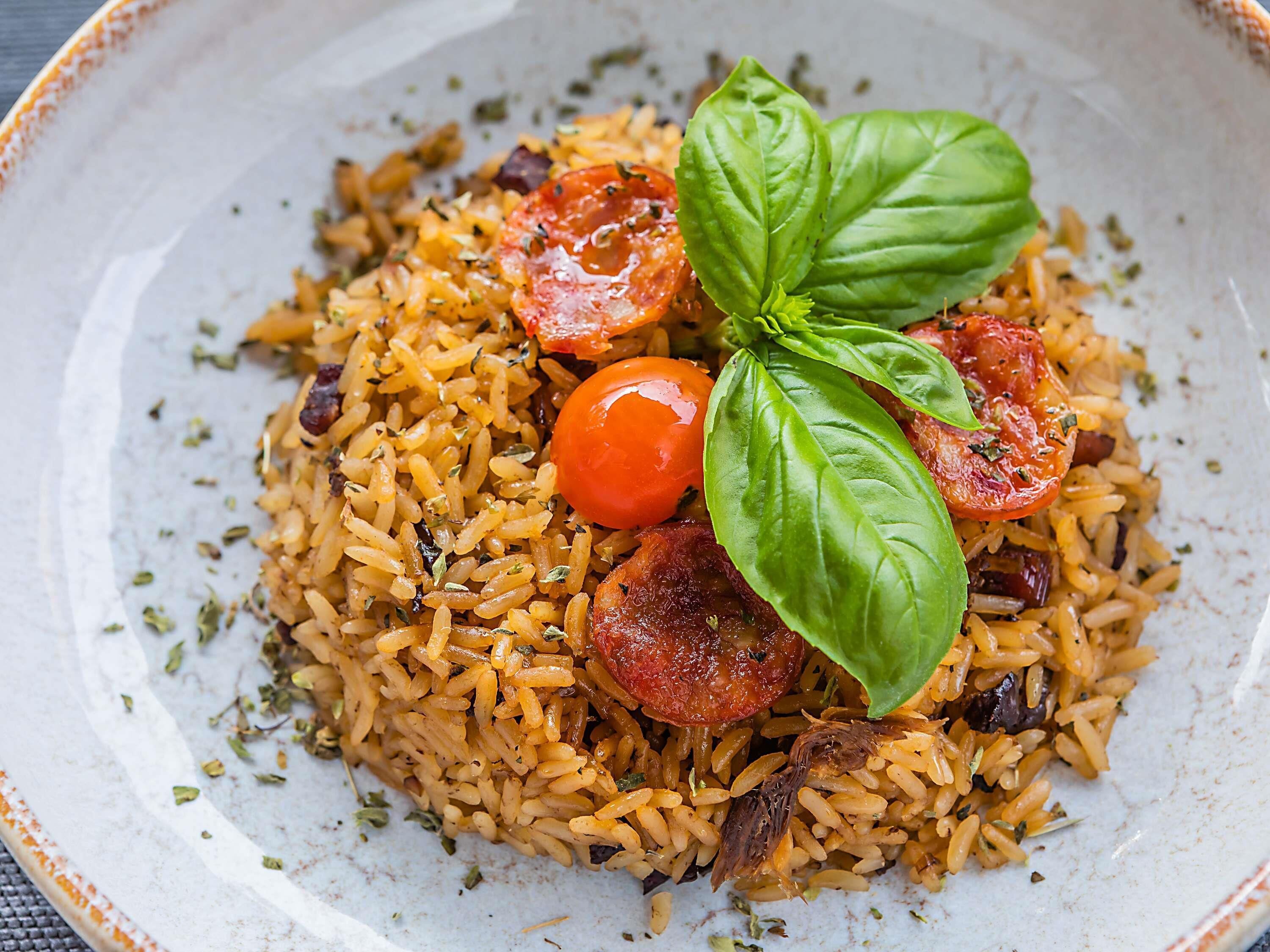 Un plato de arroz sazonado con tomate y albahaca.