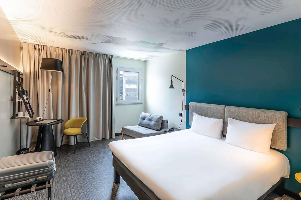 Een hotelkamer met een bed, een stoel, een bureau, een lamp en een raam.