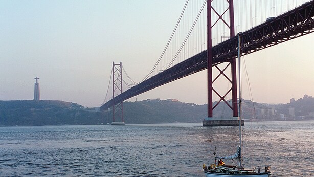 Un bote en un río con un puente grande al fondo.