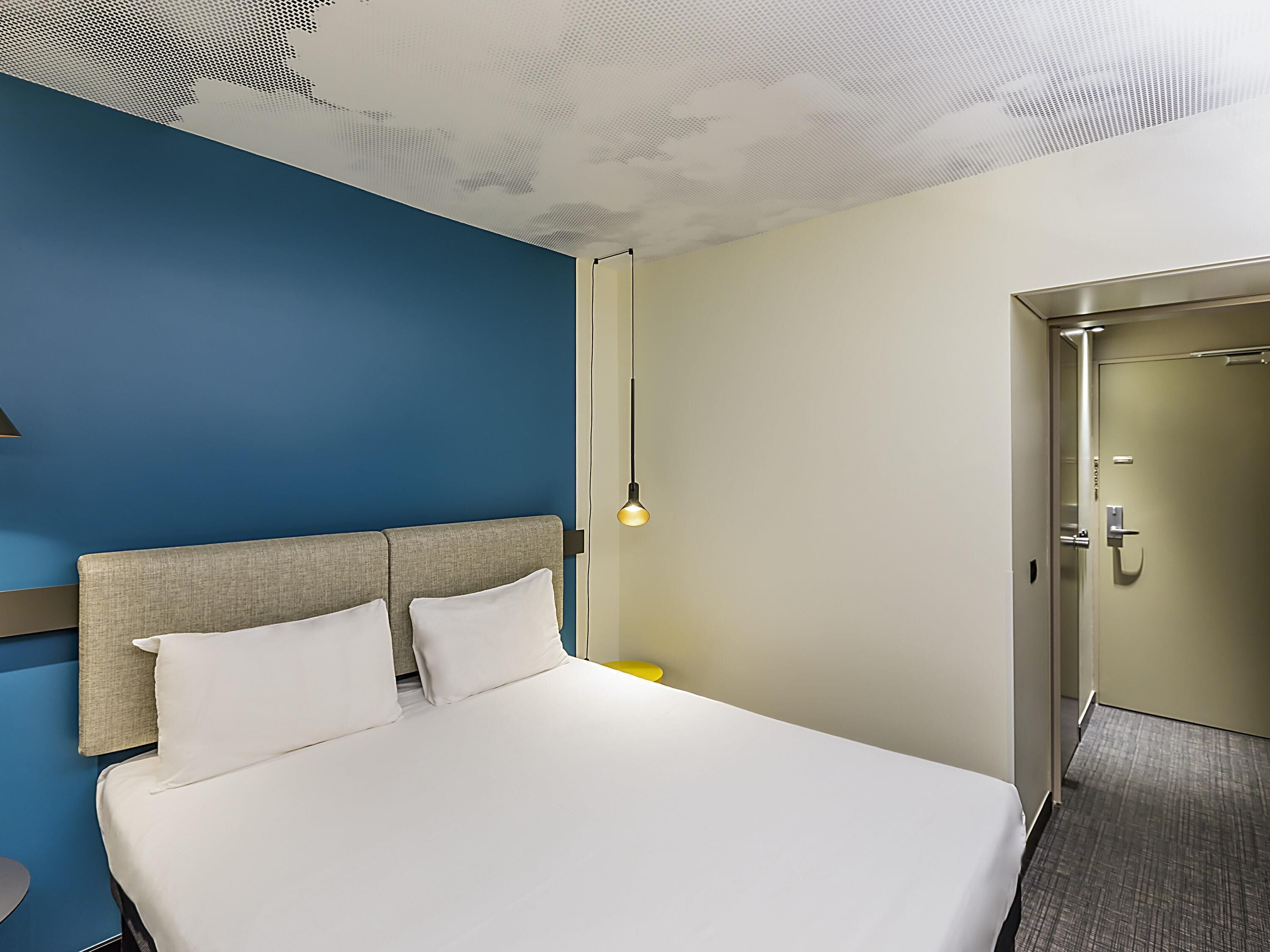 A hotel room with a large bed, a headboard, a wall-mounted light, and a door.