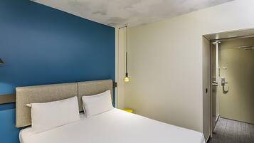 A hotel room with a large bed, a headboard, a wall-mounted light, and a door.