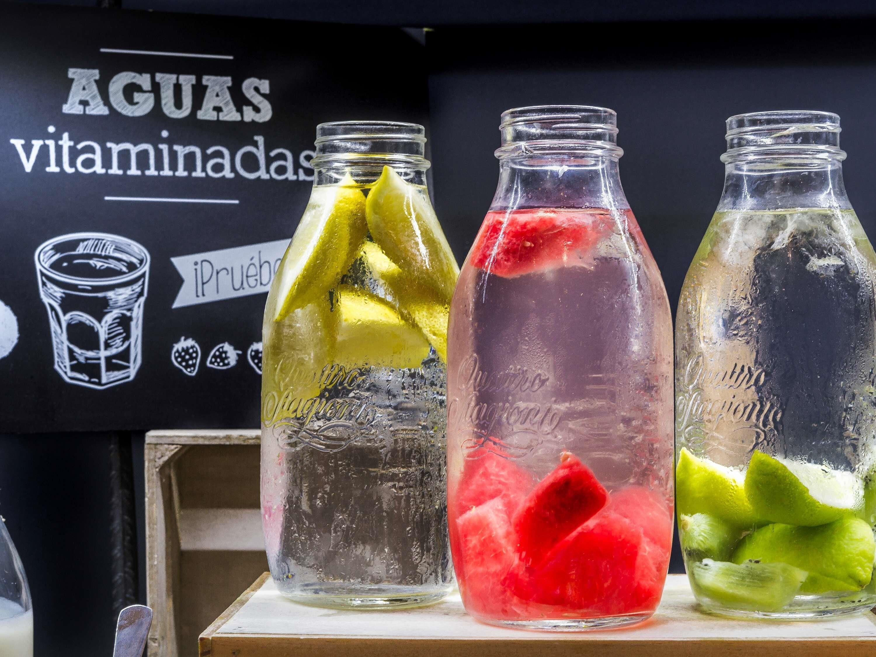 Trois bouteilles en verre contenant différents liquides de couleurs variées et des tranches de fruits, disposées sur une surface en bois.
