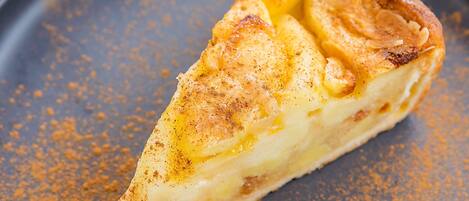 A slice of pie with a golden-brown crust, dusted with a spice, on a dark plate.