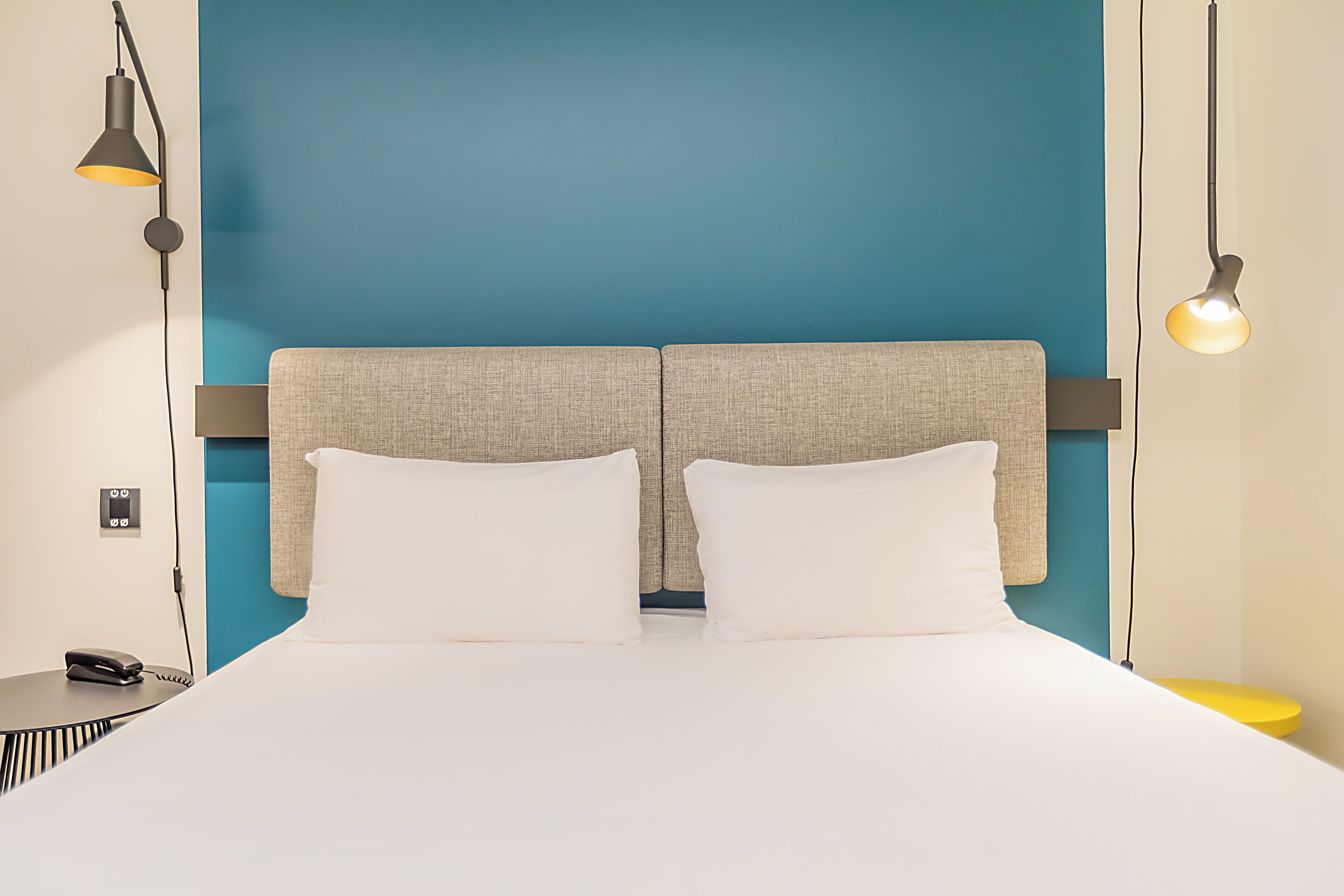 A bed with a headboard, two bedside tables, and a wall-mounted phone.