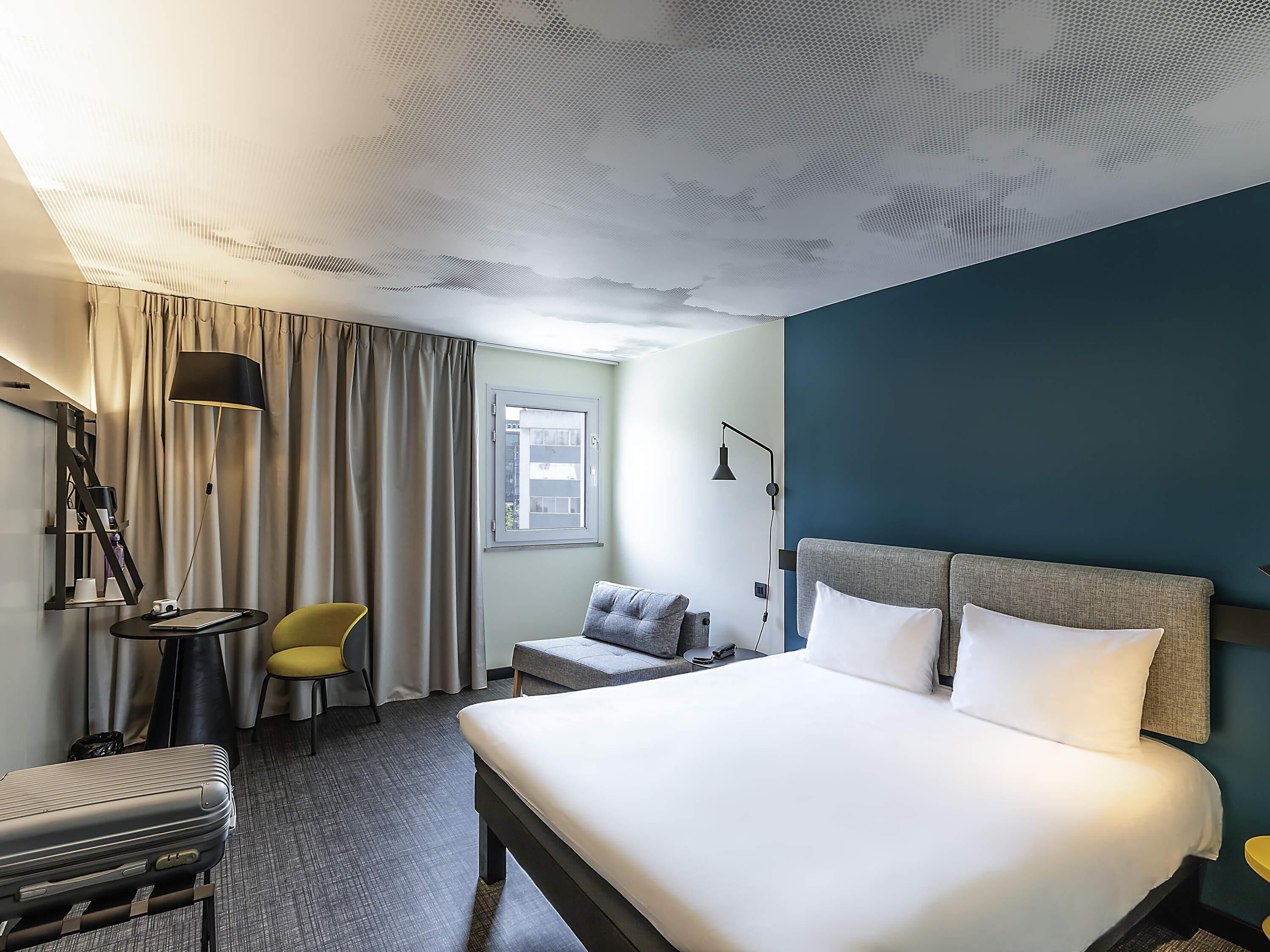 Hotellihuone, jossa on sänky, työpöytä, tuoli, lamppu ja ikkuna.