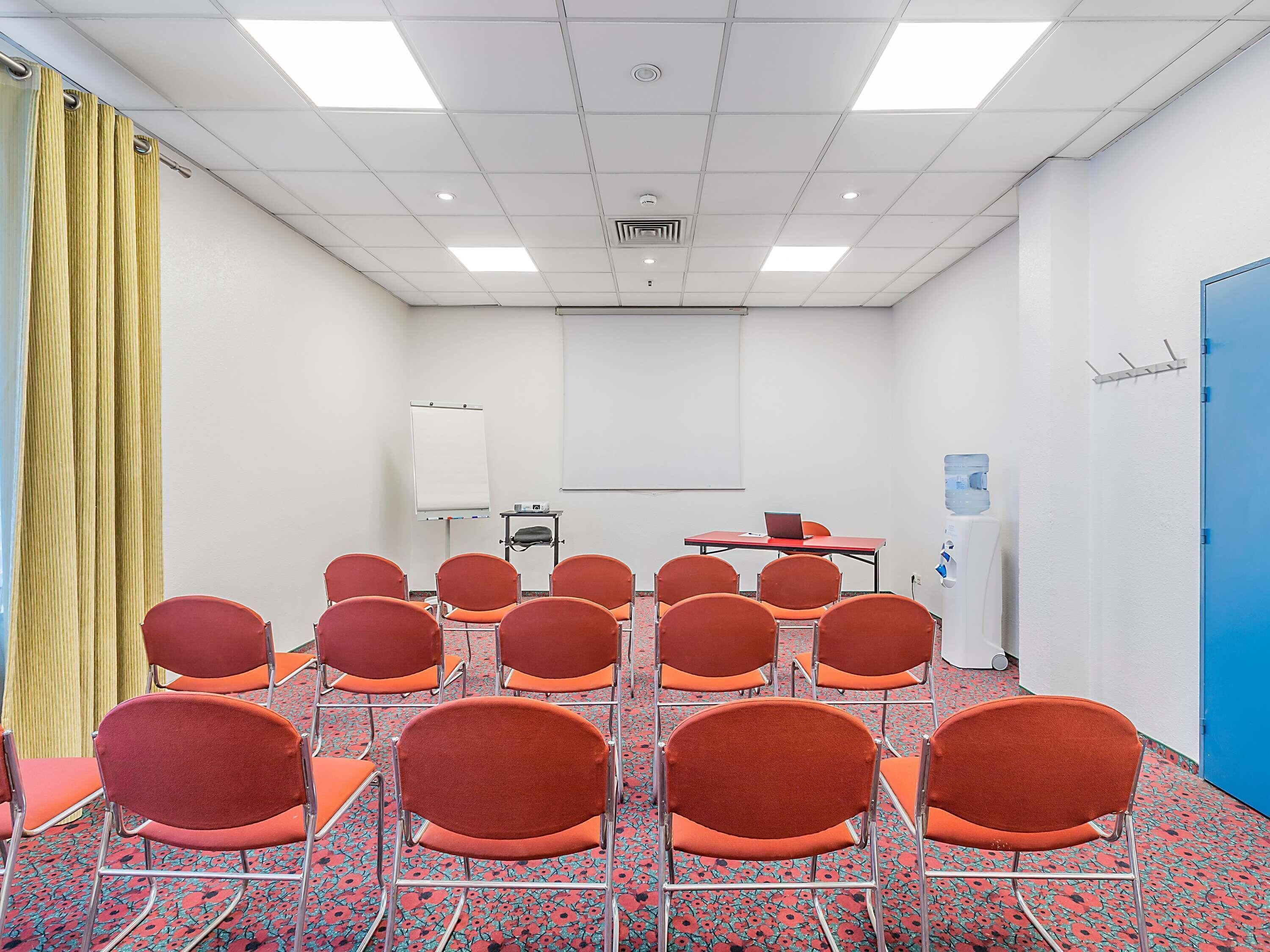 A conference room with rows of orange chairs, a whiteboard, a projector, and a water dispenser.