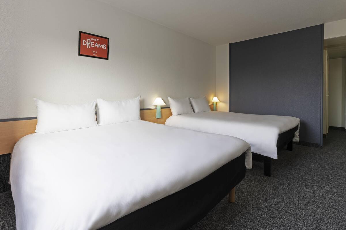 A hotel room with two beds, a nightstand with a lamp, a framed sign on the wall, and a carpeted floor.