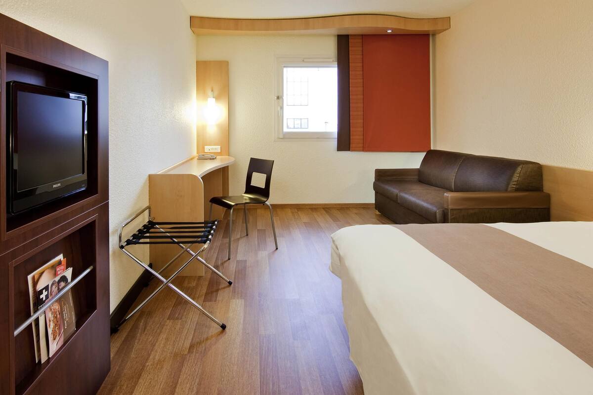 A hotel room with a bed, a desk with a chair, a television, and a window.