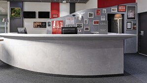 A modern reception area with a curved counter, framed pictures on the walls, and a 'Priority Welcome' sign. - ibis Paris Pantin Eglise (Pantin)