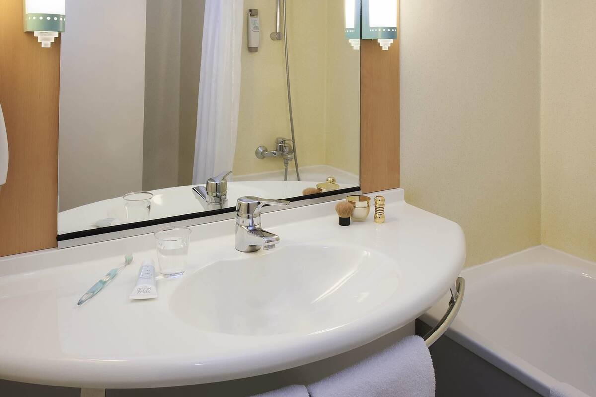 A bathroom with a white sink, a mirror, a shower, and a towel.
