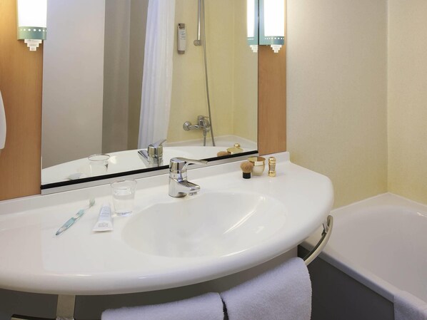 A bathroom with a white sink, a mirror, a shower, and a towel.