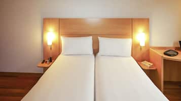 Una cama doble con dos almohadas, mesitas de noche con lámparas, una pequeña mesa con un libro y un teléfono, y un cabecero de madera.