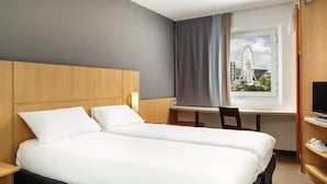 A hotel room with two beds, a desk, a chair, a TV, and a window with a view of a Ferris wheel. - ibis London Thurrock M25 (Grays)