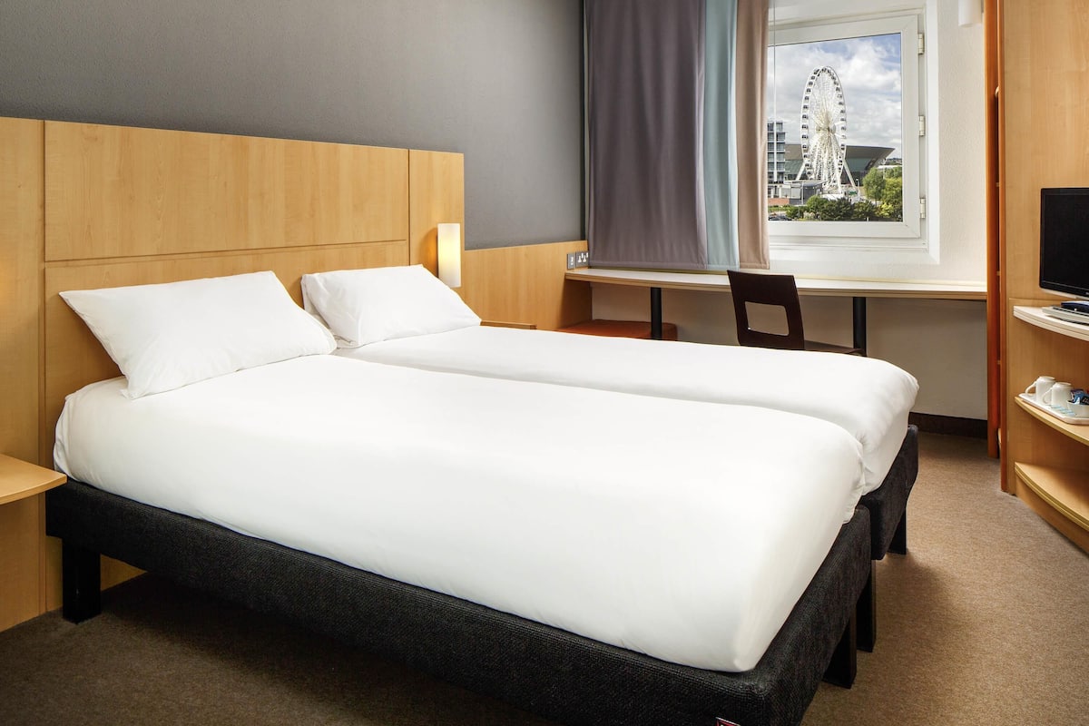A hotel room with two beds, a desk, a chair, a TV, and a window with a view of a Ferris wheel.