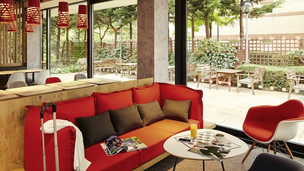 A red sofa with a magazine, a suitcase, and a table with a drink and a cup. - ibis London Thurrock M25 (Grays)