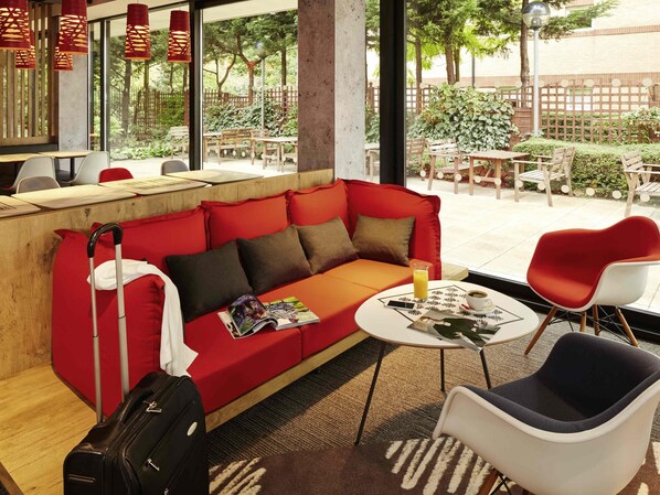 A red sofa with a magazine, a suitcase, and a table with a drink and a cup.