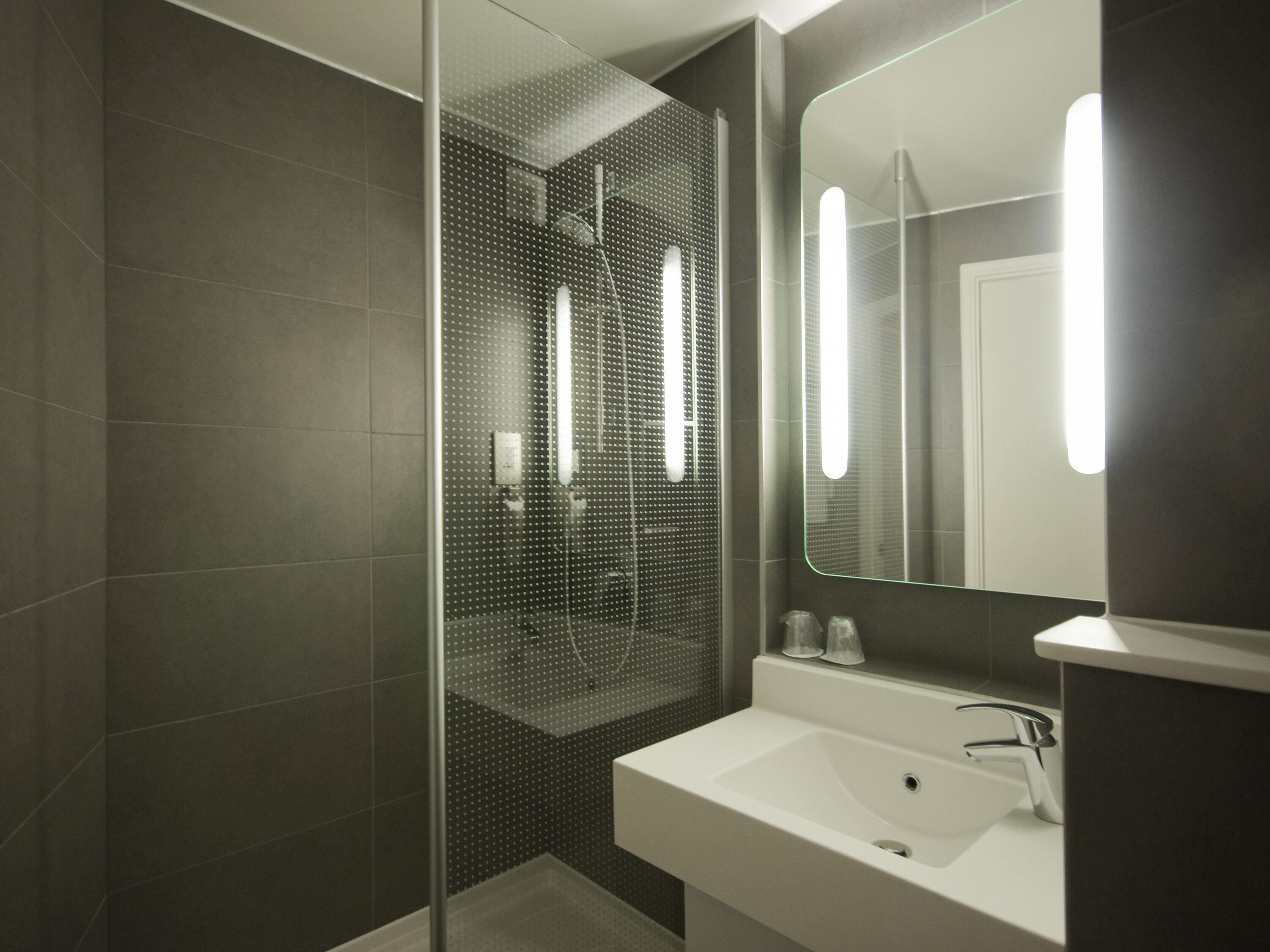 A modern bathroom with a glass shower enclosure, a white sink, and a large mirror with integrated lighting.