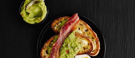 Un piatto con pane tostato, bacon e uovo sodo, accompagnato da una ciotola di guacamole.