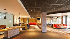 A modern reception area with a reception desk, seating area, and large windows providing natural light. - ibis London Thurrock M25 (Grays)