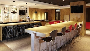 A modern bar area with a long wooden counter, multiple bar stools, and a variety of bottles and glasses on shelves. - ibis London Thurrock M25 (Grays)